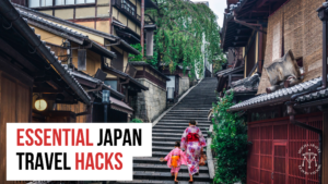 Traditional Japanese street scene with wooden houses and a steep stone staircase. A woman in a pink kimono and a child in a matching outfit are walking up the steps. The lush greenery and classic architecture capture the essence of Japan. Overlay text reads 'Essential Japan Travel Hacks' with the Mocha Travel logo