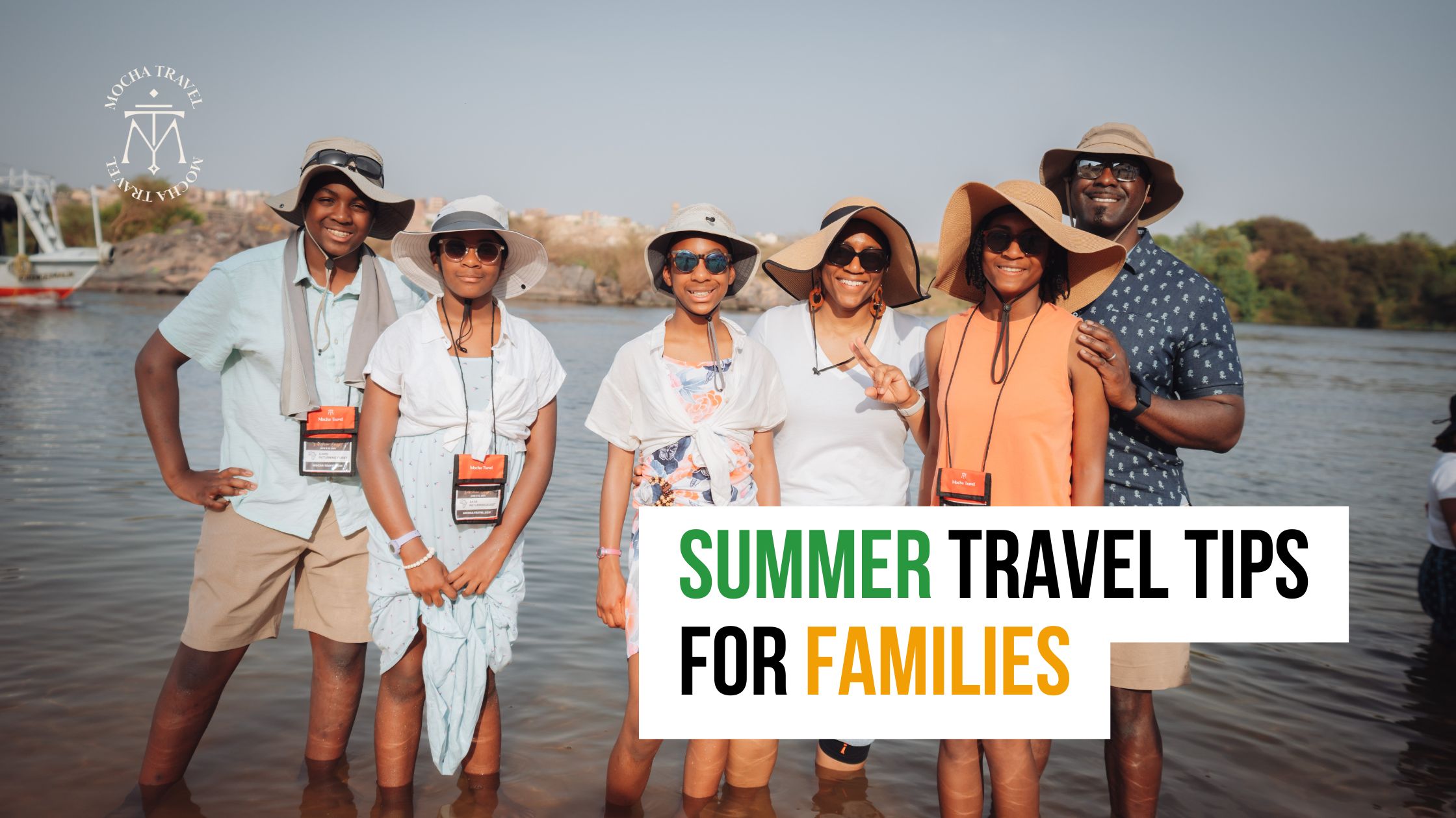A smiling family in sunhats and Mocha Travel lanyards stands in shallow water with "Summer Travel Tips for Families